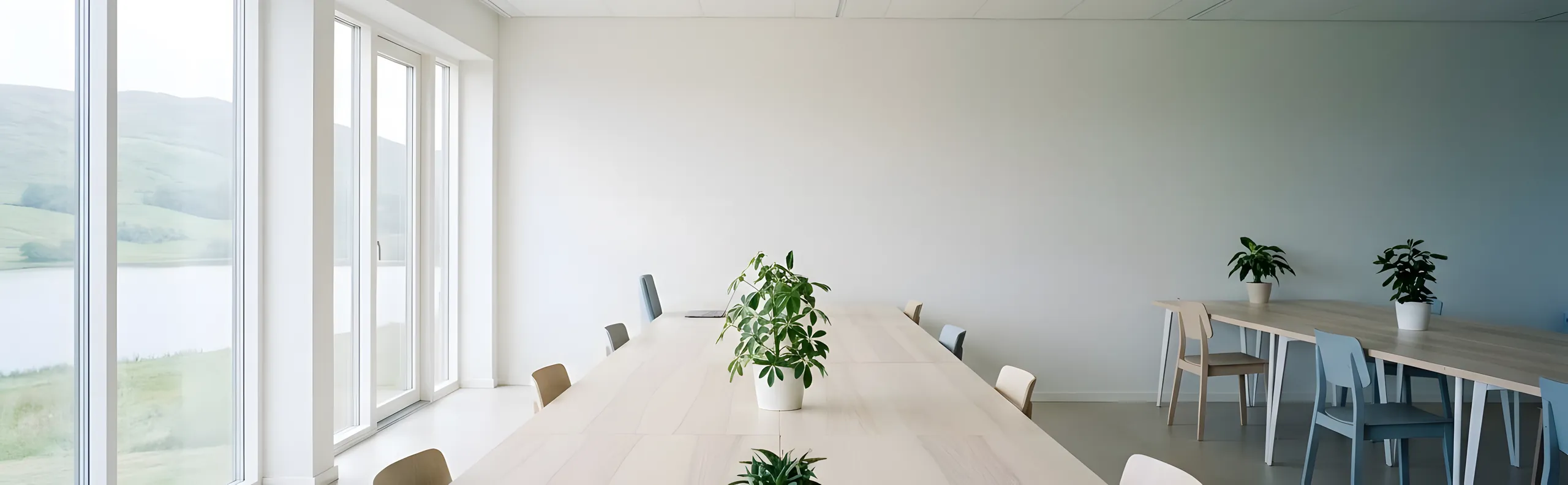 Helles Büro mit langen Holztischen und Blick über Wiesen auf einen See