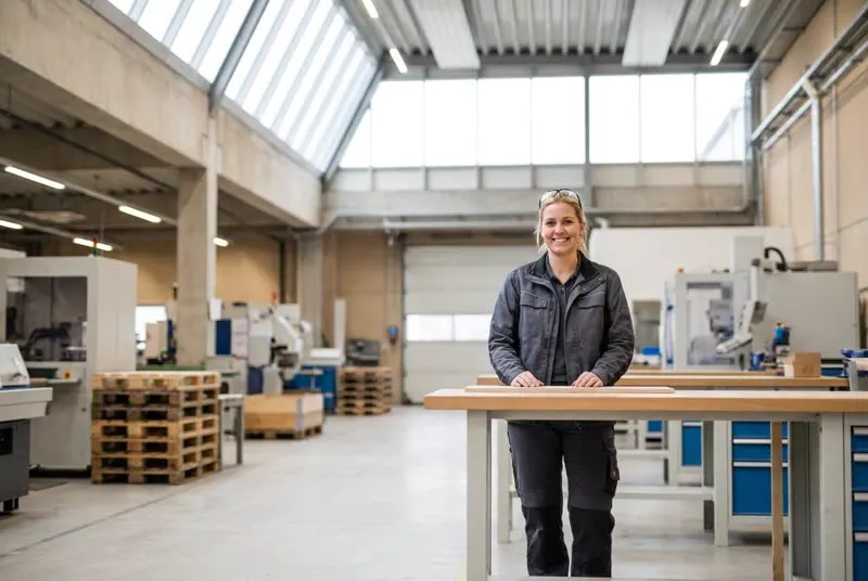 Produktionsmitarbeiterin in einer hellen Halle, sie sieht in die Kamera